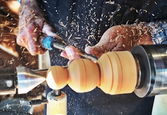 Hands operating a wood lathe, meticulously crafting and shaping a piece of wood amidst flying wood shavings.