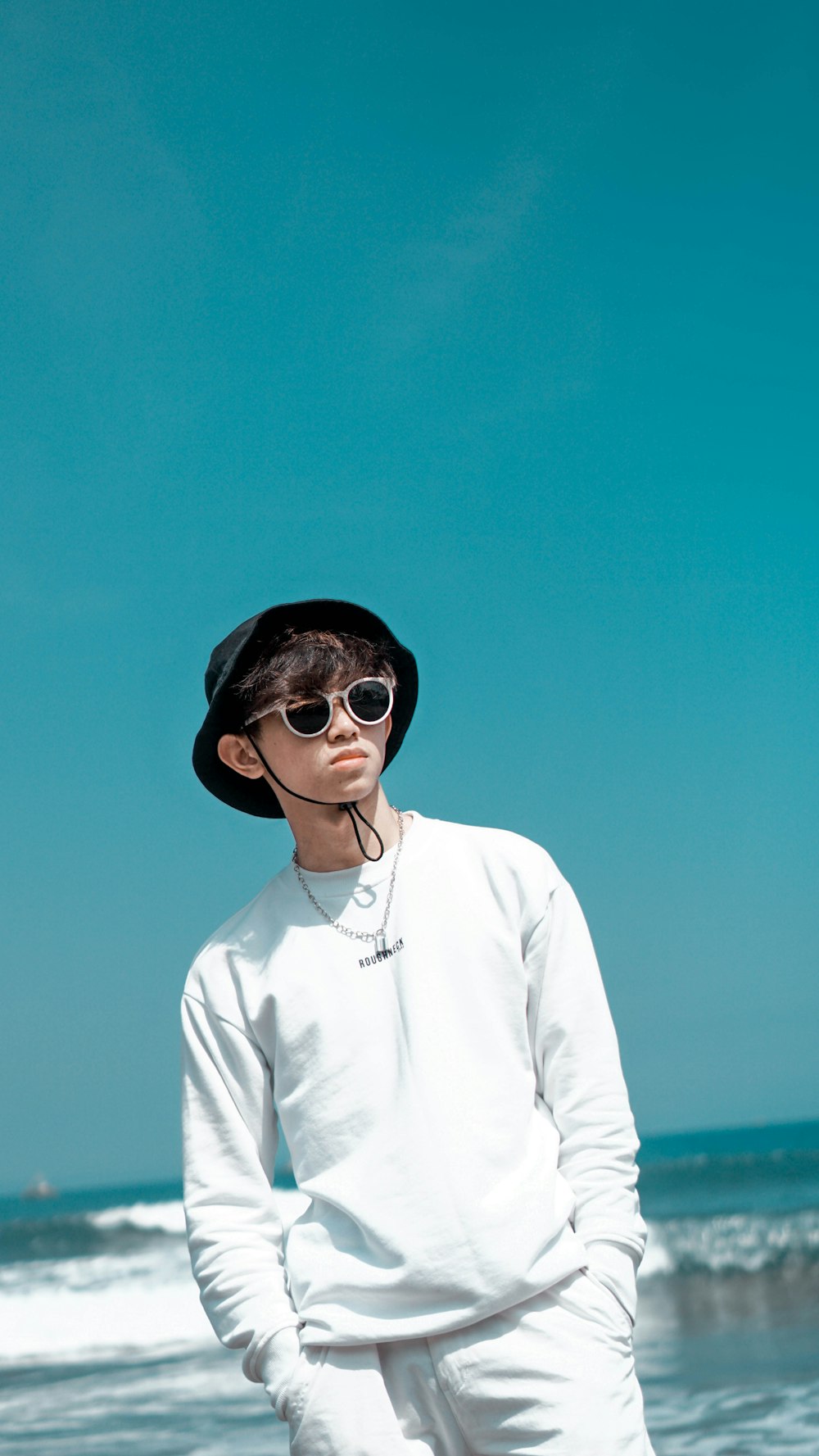 a man standing on the beach wearing a hat and sunglasses