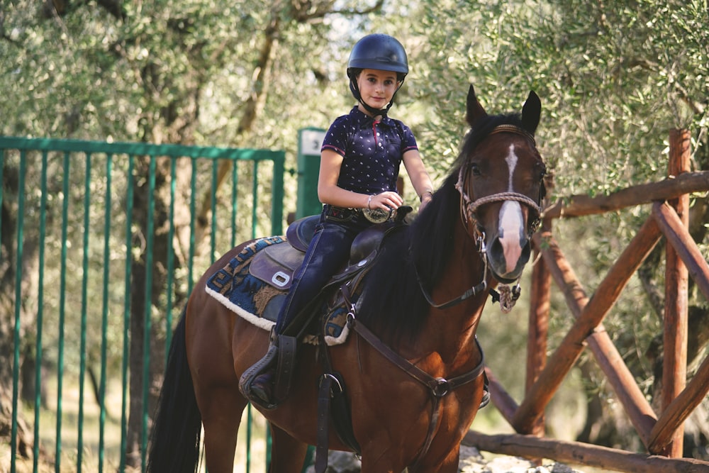 a young girl riding on the back of a brown horse