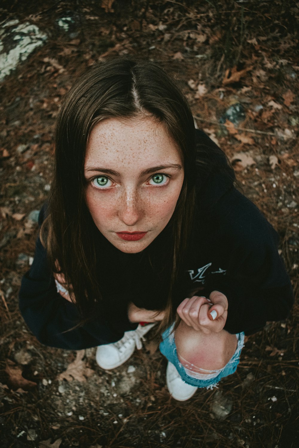 a woman with freckled hair and blue eyes sitting on the ground