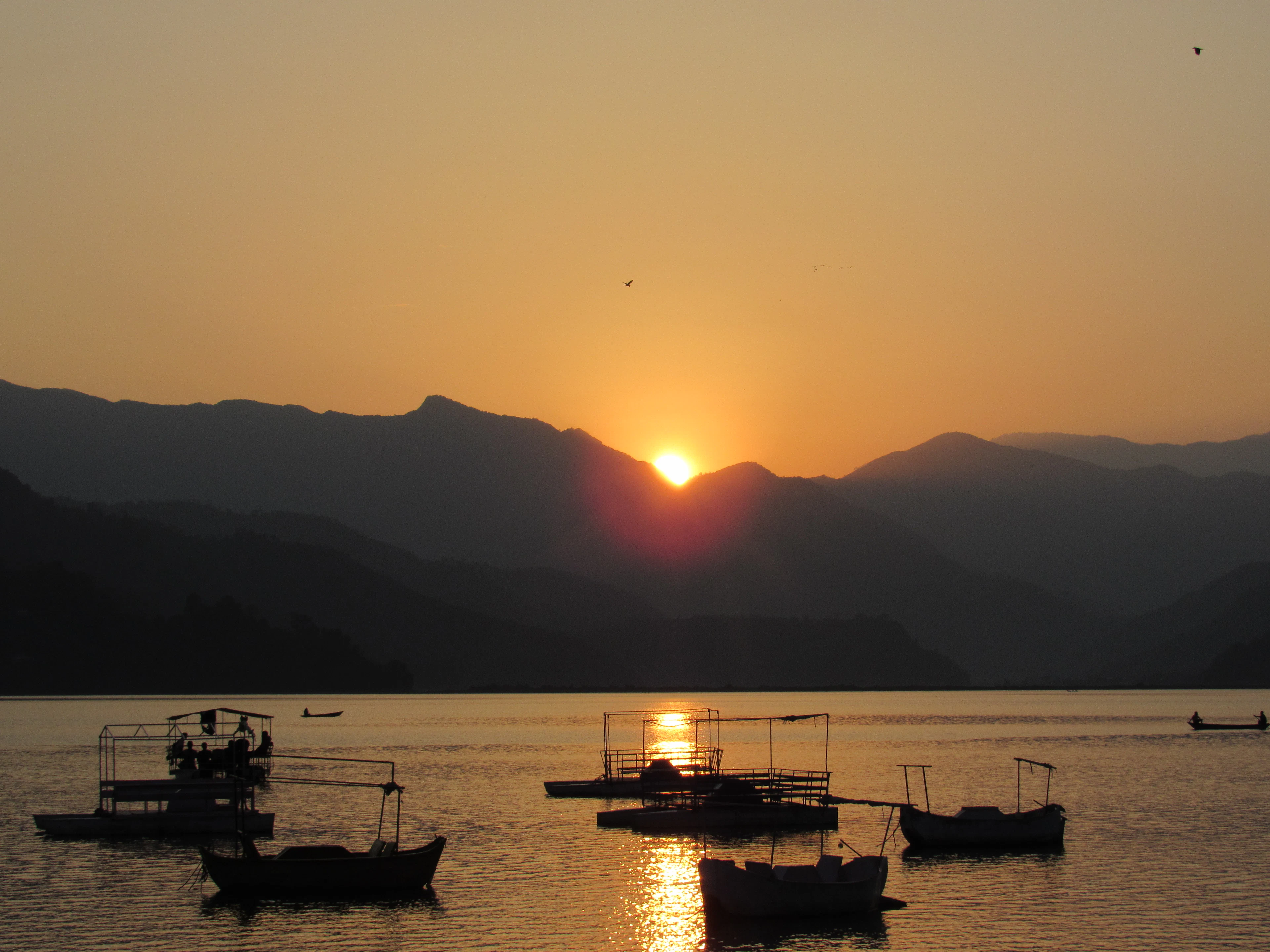 Sunset over the hills and boats on the still water of Phewa Lake, Pokhara
