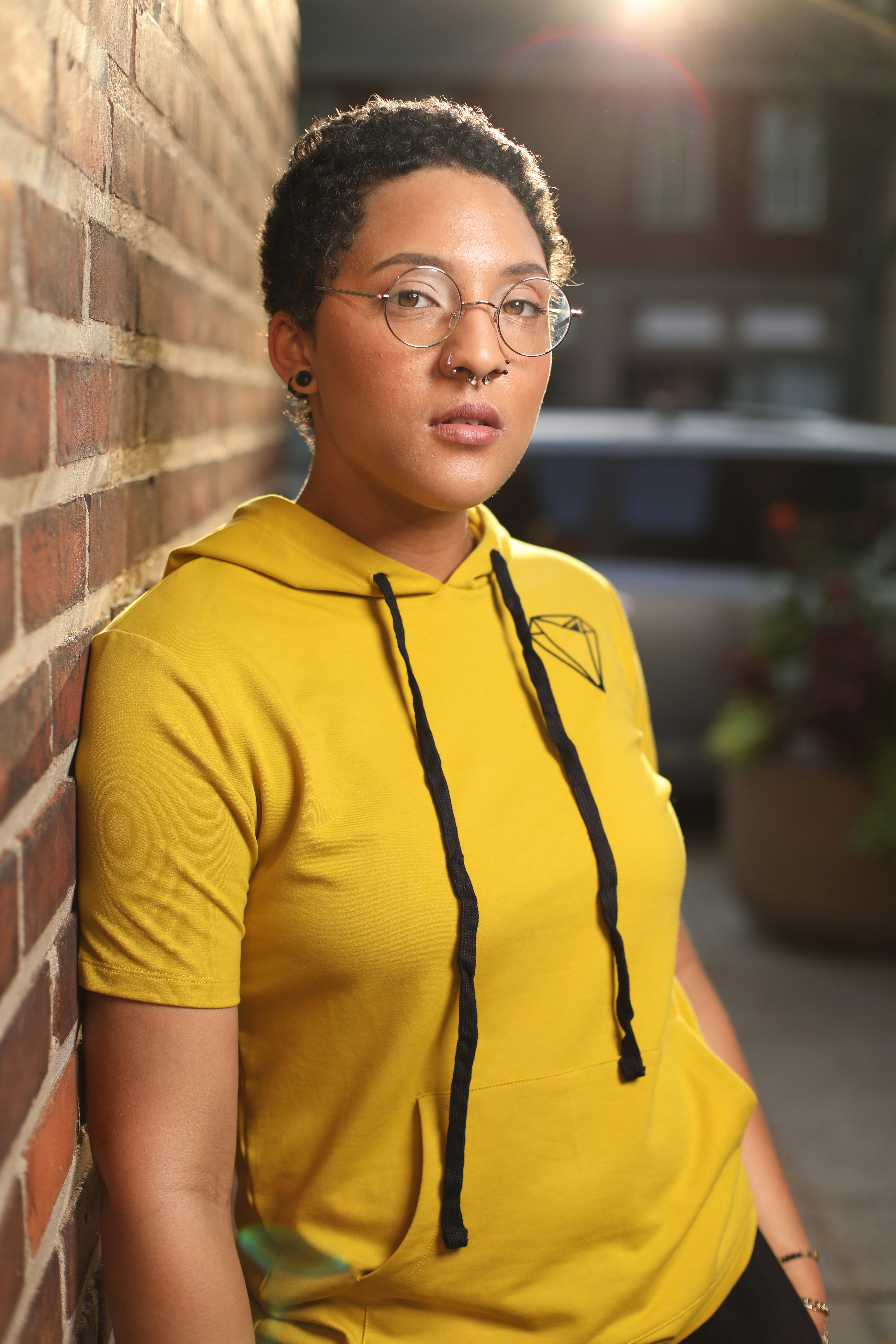 a woman wearing glasses leaning against a brick wall