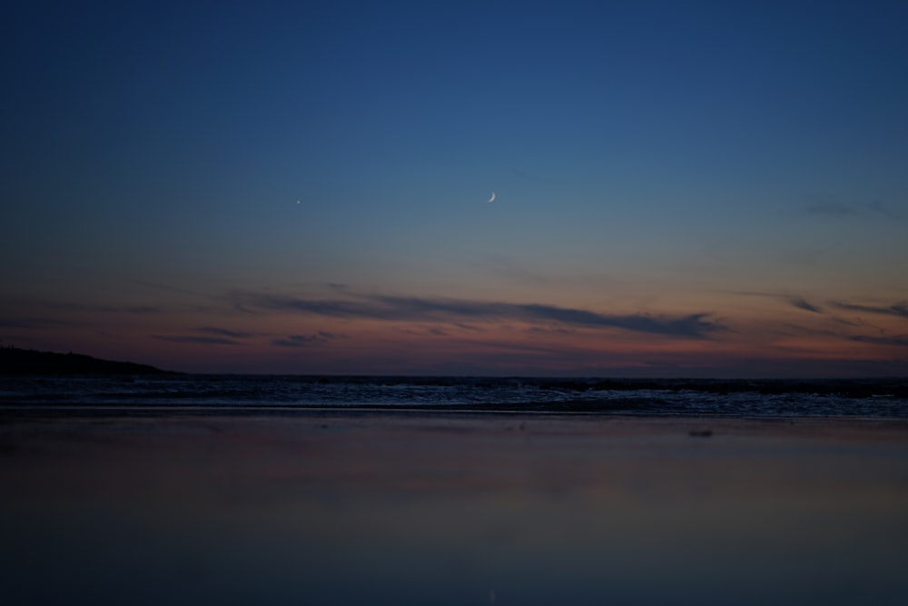 the moon is setting over the water at the beach