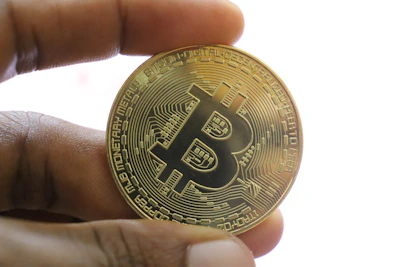 Close-up of hands holding a physical bitcoin token against a violet purple background.