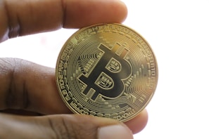 Close-up of hands holding a physical bitcoin coin over a digital blockchain interface.