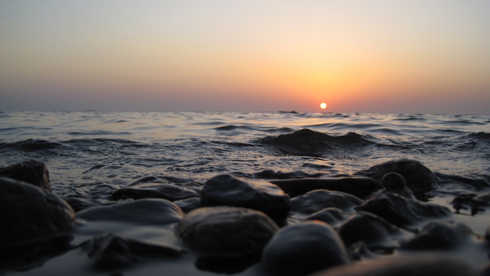 a sunset over the ocean with rocks in the foreground