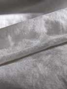 A close-up view of a piece of fabric with a soft texture, displaying a gentle sheen. The material appears to be folded, forming subtle shadows and highlights on its surface.