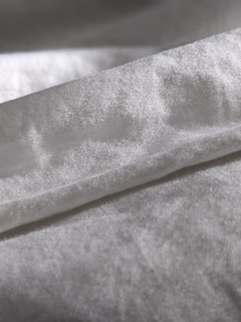 A close-up view of a piece of fabric with a soft texture, displaying a gentle sheen. The material appears to be folded, forming subtle shadows and highlights on its surface.