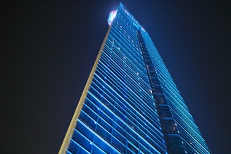 A sleek futuristic office building glowing with blue lights at dusk.