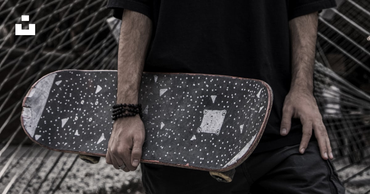 A man holding a skateboard in front of a fence photo – Free Riverside