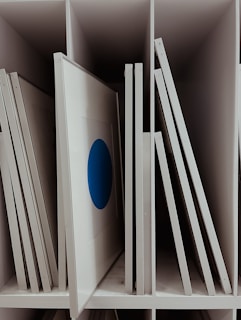 Several framed artworks are arranged vertically in storage slots. One frame features a prominent blue circle on a white background. The storage system is organized with frames labeled numerically.