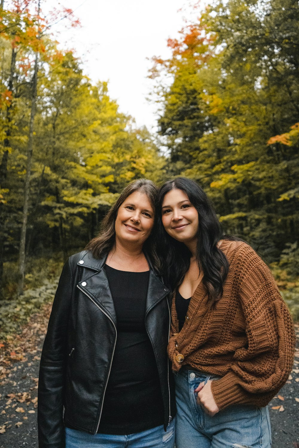 two women standing next to each other in front of trees