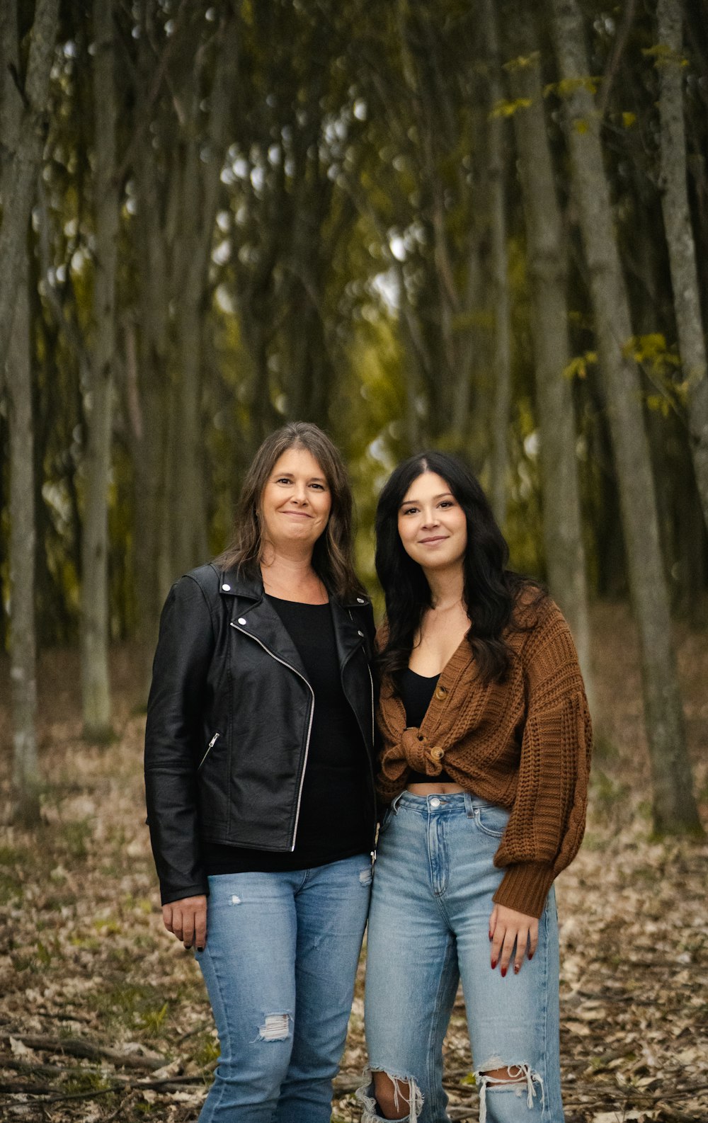 two women standing next to each other in a forest