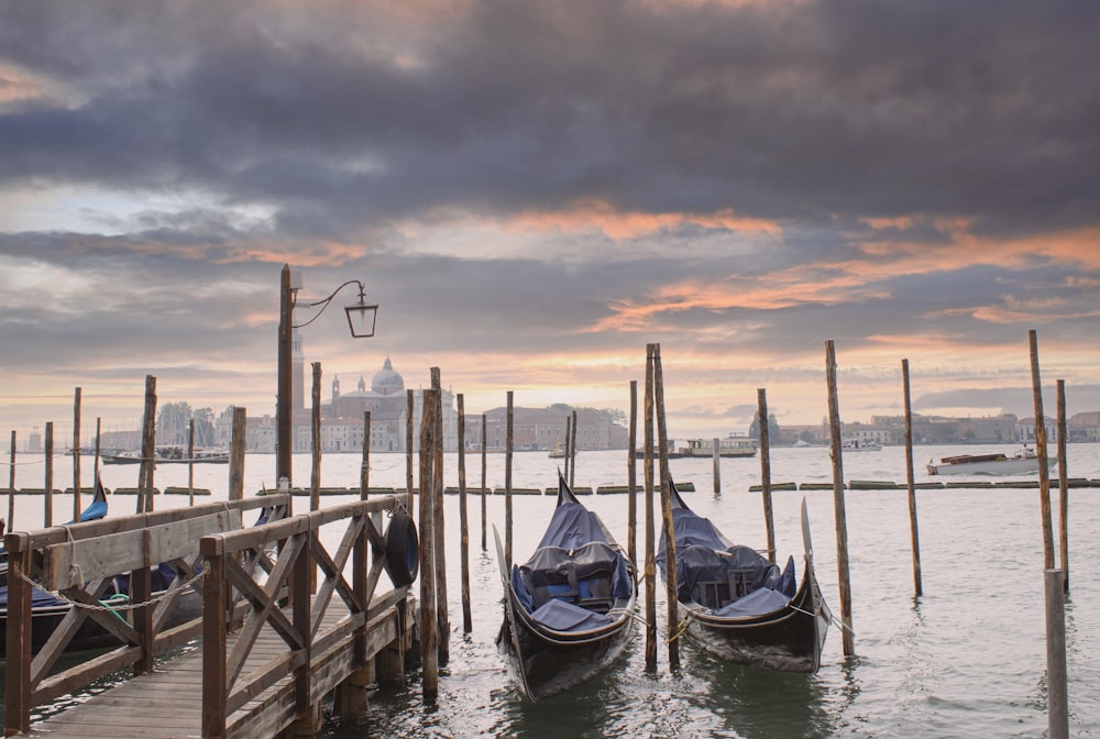 two gondolas tied to a wooden pier with a city in the background