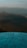 A metal compass or directional dial is mounted atop a surface, with various distances and directions inscribed on it. The background is an out-of-focus landscape, possibly featuring mountains or hills under a soft sky.