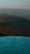 A metal compass or directional dial is mounted atop a surface, with various distances and directions inscribed on it. The background is an out-of-focus landscape, possibly featuring mountains or hills under a soft sky.