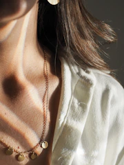 A close-up of a model wearing a delicate gold necklace paired with a chic, flowing dress in soft natural light.
