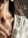 A close-up view of a woman's neck and shoulder, adorned with a delicate gold necklace featuring small round pendants. She is wearing a white textured garment and light is casting artistic shadows on her skin.