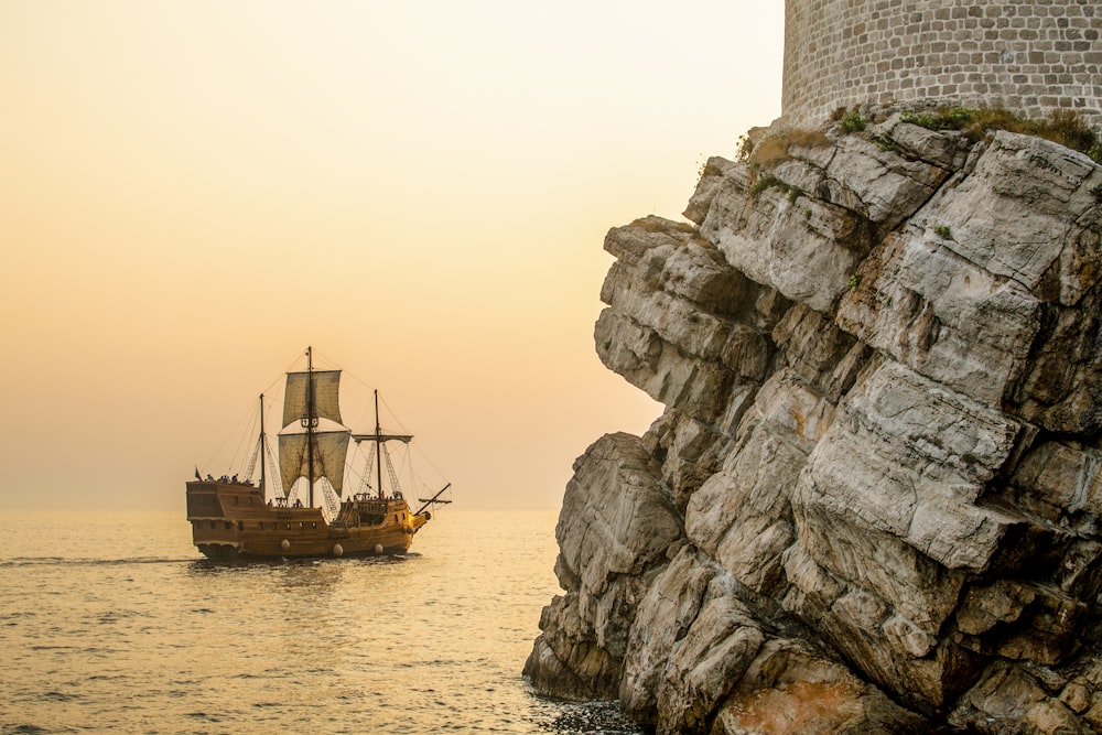 a boat sailing on the water near a rocky cliff