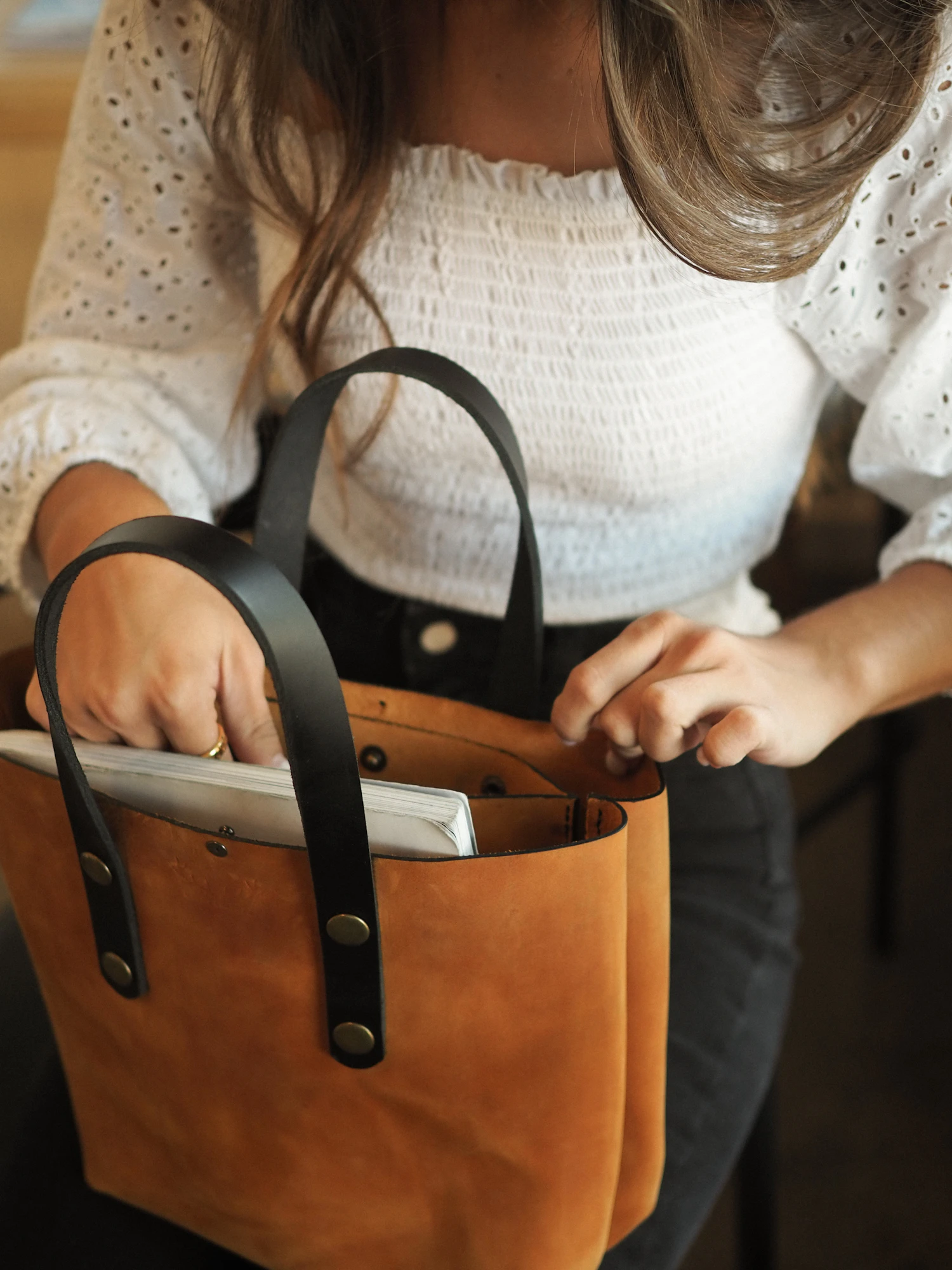 A woman sliding a laptop into a tan leather tote with black handles