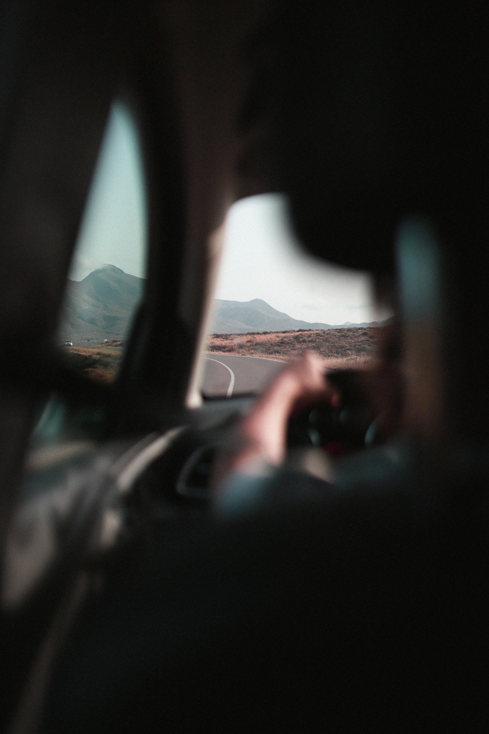 a person driving a car on a road with mountains in the background