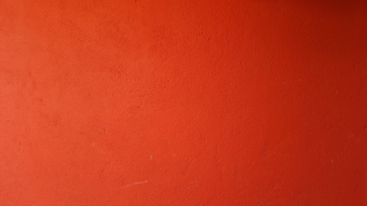 A painter carefully applying a smooth orange coat on a modern interior wall.
