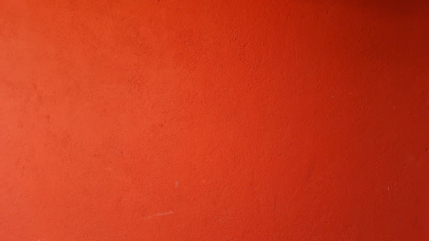 Close-up of a paintbrush applying smooth, rich orange paint on a wall surface.