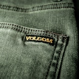 Close-up view of a textured green fabric featuring a visible seam and a small black label with gold embroidery.