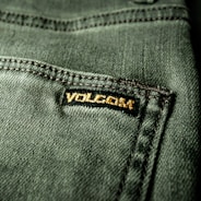 Close-up view of a textured green fabric featuring a visible seam and a small black label with gold embroidery.