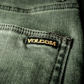 Close-up view of a textured green fabric featuring a visible seam and a small black label with gold embroidery.