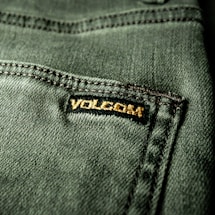 Close-up view of a textured green fabric featuring a visible seam and a small black label with gold embroidery.