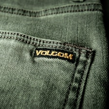 Close-up view of a textured green fabric featuring a visible seam and a small black label with gold embroidery.