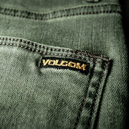 Close-up view of a textured green fabric featuring a visible seam and a small black label with gold embroidery.