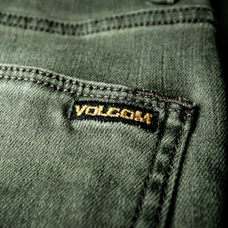 Close-up view of a textured green fabric featuring a visible seam and a small black label with gold embroidery.