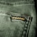 Close-up view of a textured green fabric featuring a visible seam and a small black label with gold embroidery.