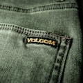Close-up view of a textured green fabric featuring a visible seam and a small black label with gold embroidery.