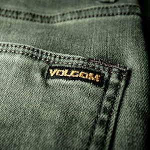 Close-up view of a textured green fabric featuring a visible seam and a small black label with gold embroidery.