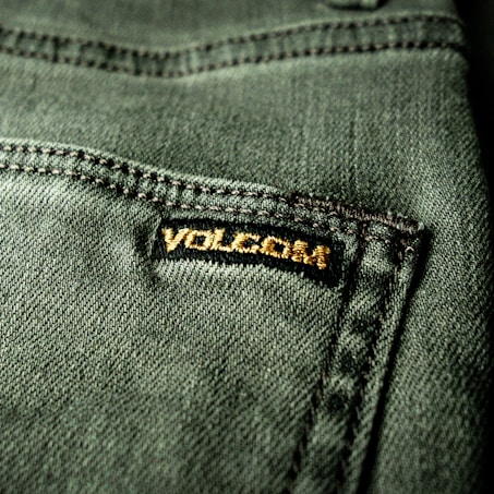 Close-up view of a textured green fabric featuring a visible seam and a small black label with gold embroidery.
