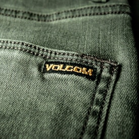 Close-up view of a textured green fabric featuring a visible seam and a small black label with gold embroidery.