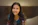 A warm, natural portrait of a smiling young woman in a cozy, softly lit room.