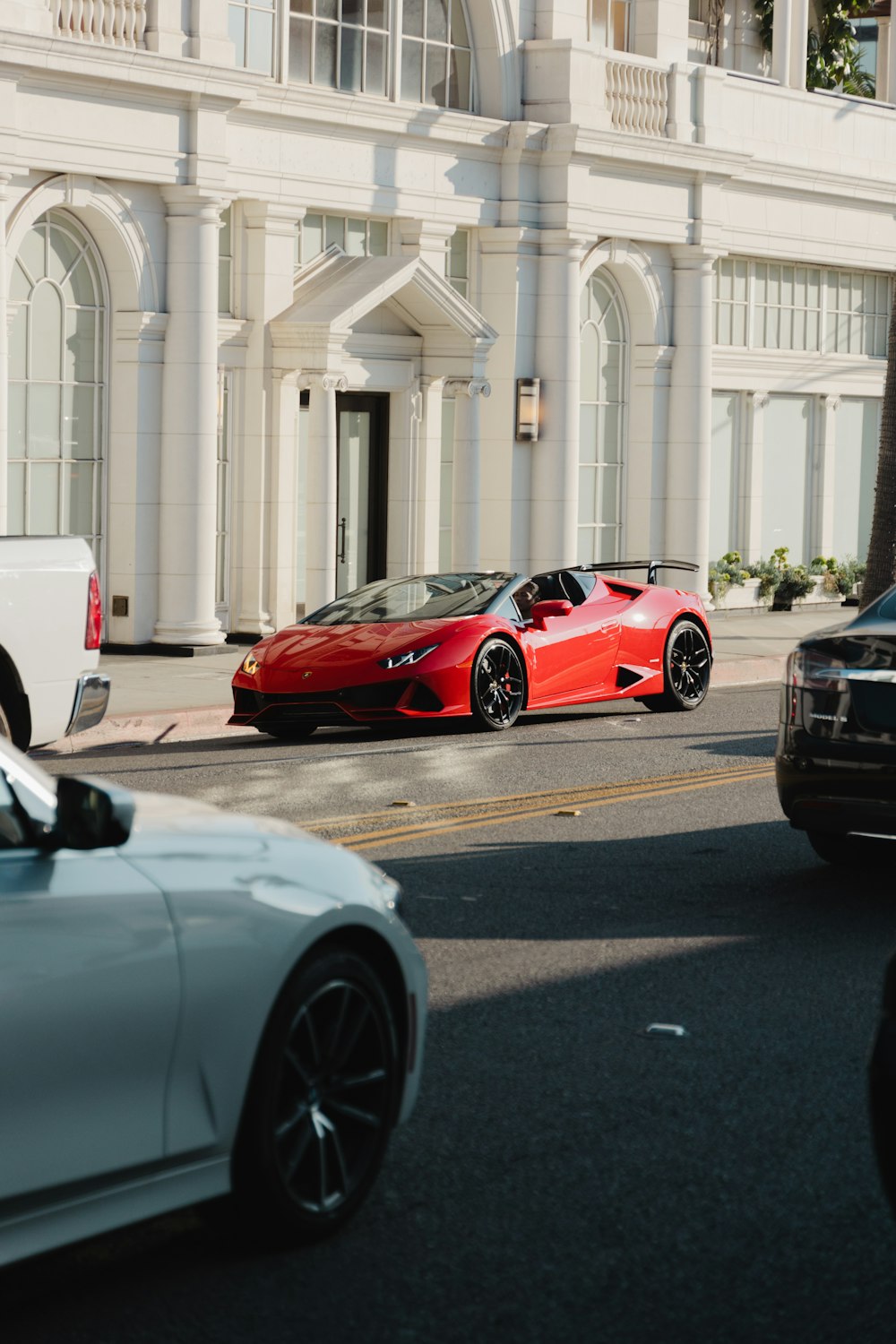 a red sports car driving down a street next to a white building