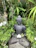 A peaceful ceramic figure seated in meditation surrounded by greenery.