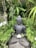 A peaceful ceramic figure seated in meditation surrounded by greenery.