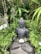 A peaceful ceramic figure seated in meditation surrounded by greenery.