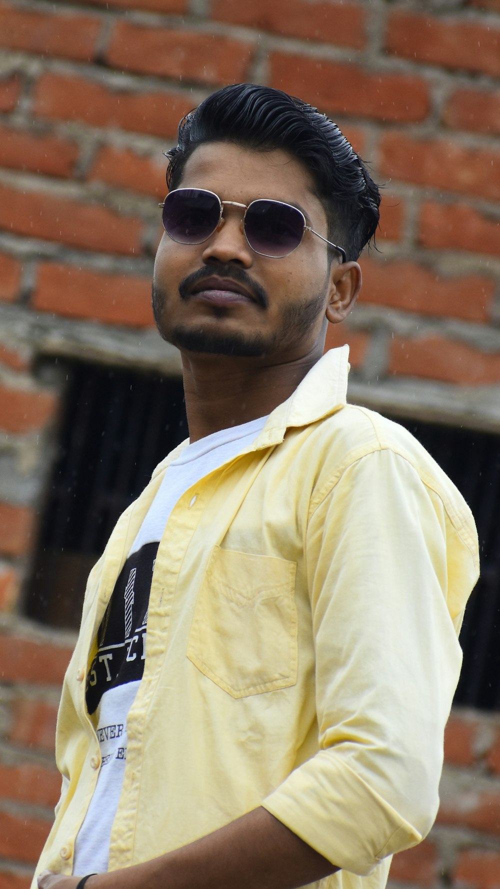 a man wearing sunglasses standing in front of a brick wall