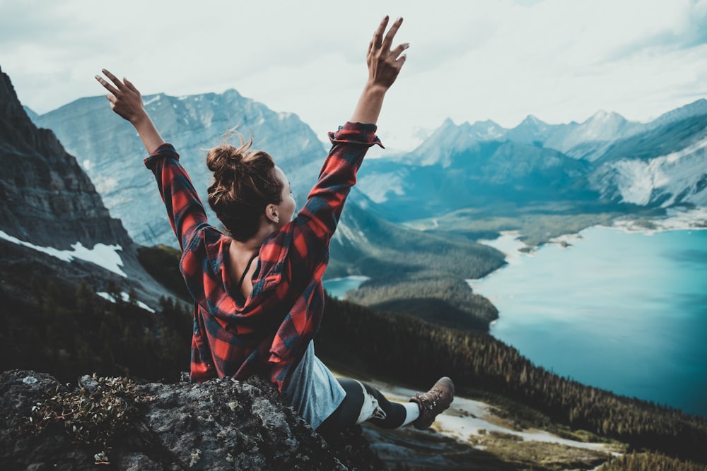 a woman sitting on top of a mountain with her hands up