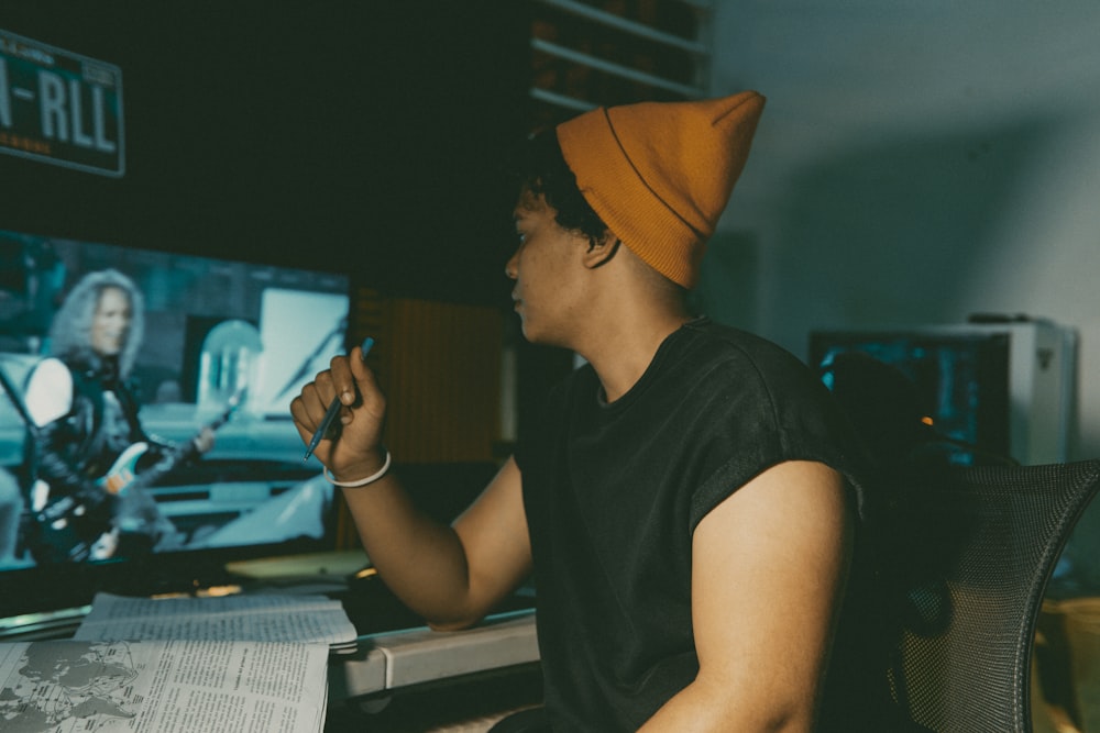 a man wearing a beanie sitting in front of a tv