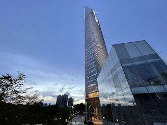 A sleek high-rise residential tower glowing at dusk with city lights in the background.