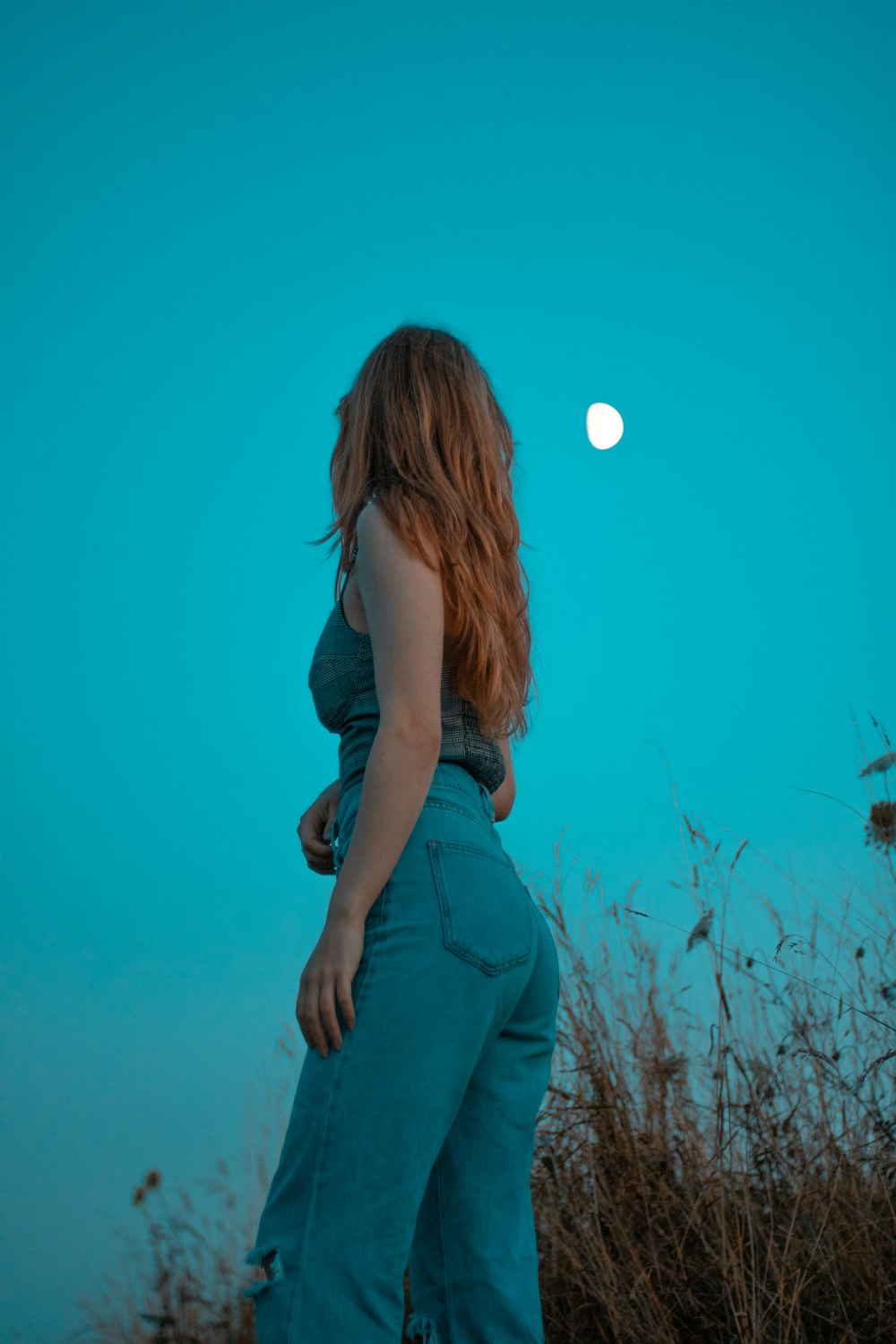 a woman standing in a field with a full moon in the background
