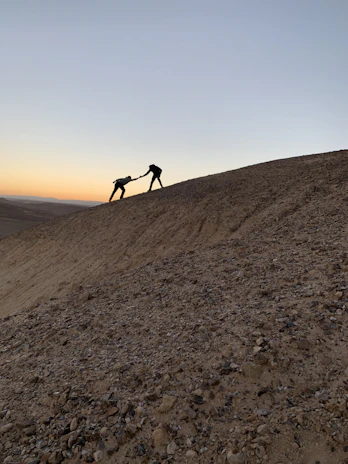 Participants helping each other climb a steep rocky incline, teamwork in action.